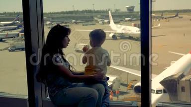 女人和男孩一起看机场的跑道，关门。 一家人在看飞机的时候等待航班。