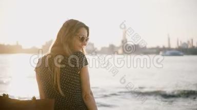 美丽的欧洲女人戴着太阳镜回头<strong>看镜头</strong>，转身离开阳光明媚的<strong>城市</strong>海滩。 享受夏日日落4K。