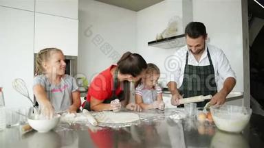 家庭有乐趣，彼此玩面粉。 快乐的父母在围裙帮助孩子做饭。