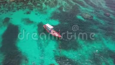 在珊瑚礁边缘的绿松石浅水中锚定的船。 鸟瞰图