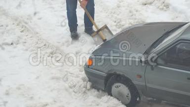 一个人从一辆被困在雪地里的车里挖了一铲雪