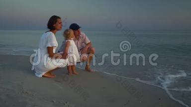 家人在海滩上散步。 父母和他们的小女儿沿着海滨散步。 父母蹲在他们身边