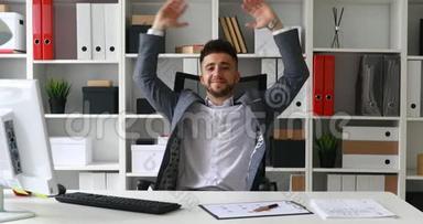 商人坐在白色办公室的桌子旁，双手抛在头后，在办公室的椅子上摇摆