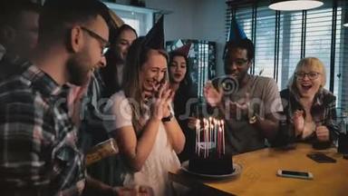 快乐的白人女孩在生日蛋糕上用蜡烛许愿。 多种族的朋友在惊喜派对慢动作。
