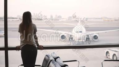 年轻的欧洲女商人站在机场候机厅窗口看，看和使用智能手表。