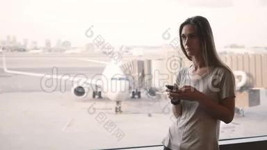 站在机场候机楼窗口附近的年轻欧洲妇女看着<strong>电话</strong>和智能<strong>手表</strong>感到沮丧和沮丧。