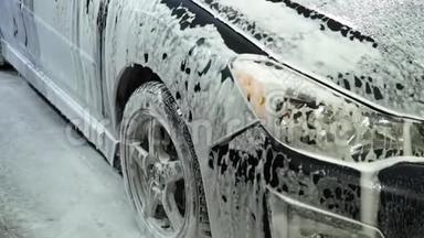 洗车。 洗车机清洗汽车。 车上覆盖着白色的冲洗泡沫.. 特写镜头。