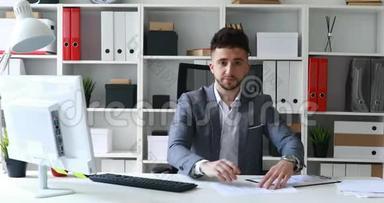 年轻男子灰色夹克坐在白色办公室的桌子上，提供文件