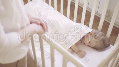 一个穿着白色衣服的女人站在<strong>婴儿床</strong>旁边，<strong>婴儿床</strong>上睡着一个小孩