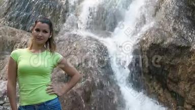 一个<strong>女人</strong>站在<strong>瀑布</strong>的背景上。 快速的<strong>瀑布</strong>沿着岩石流下来。 一个美丽的微笑女孩旁边