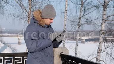 穿着蓝色羽绒服，带着皮帽的人用<strong>手机</strong>上网，在冬<strong>季</strong>公园聊天。