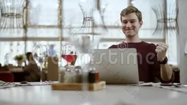 一个年轻的商人坐在一家咖啡馆的桌子旁，用<strong>iphone</strong>一边笑一边看着过路人
