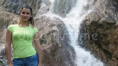 一个女人站在瀑布的背景上。 快速的瀑布沿着岩石流下来。 一个美丽的微笑女孩旁边