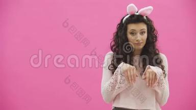 复活节的节日。复活节兔子耳朵上带着微笑的年轻女子在粉色背景上跳来跳去看着复制品