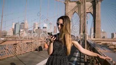 快乐的年轻白种人女士戴着老式太阳镜在电话里交谈，在布鲁克林大桥4K的风中吹着头发。