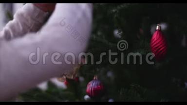 把圣诞装饰品挂在有圣诞灯的树上。 小女孩的手装饰圣诞树，特写