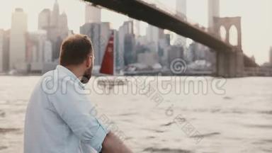 成功的白人自由商人站在纽约布鲁克林大桥下的河堤旁，<strong>红船</strong>经过