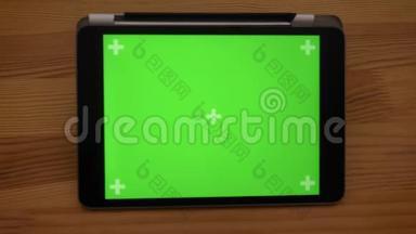 慢慢地拉开水平平板电脑的特写镜头，在木制桌子背景上有绿色的屏幕。