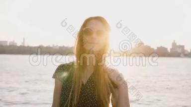 快乐休闲的白种人女孩，戴着时尚的太阳镜，在相机上摆姿势，纽约日落天际线和背景4K的河流。