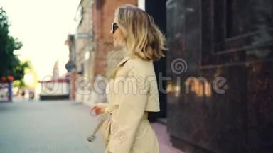 微笑的年轻女子，穿着时髦的外套，走在街上，转向相机，看着她的慢镜头