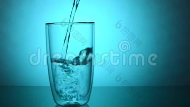 将新鲜的饮用水<strong>倒入</strong>蓝色背景的玻璃<strong>杯中</strong>