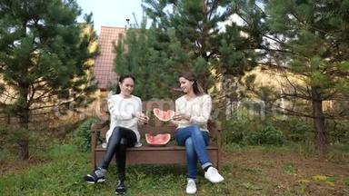 公园里有两个女孩在吃西瓜。 慢动作视频生活方式。 女孩和西瓜的概念