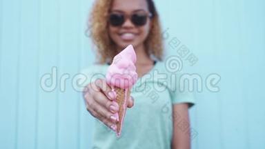 戴墨镜<strong>的</strong>快乐黑人女孩在蓝墙背景下展示了粉红色<strong>的</strong>融化冰淇淋