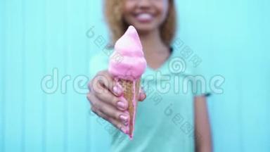 快乐的黑人女孩展示了粉红色融化的冰淇淋，然后开始在蓝色的墙壁背景下吃它