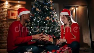 幸<strong>福</strong>的一对夫妇正坐在家里客厅的一块蓬松的地毯上。 一个男人正在给女孩<strong>送</strong>圣诞礼物。
