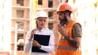 戴着防护头盔的妇女与戴着头盔和穿着防护背心的建筑工人沟通