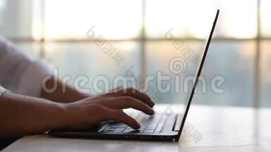 特写，男人的手在笔记本电脑键盘上打字，在窗户的背面