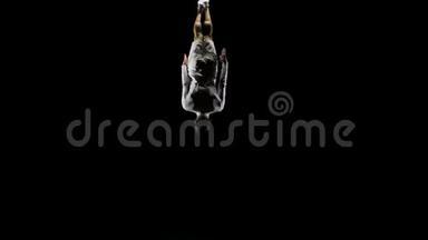 穿着白色衣服、黑色背景的英俊男体操运动员，在蹦床上缓慢地跳跃，表演翻转和跳跃