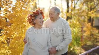 在一个美丽的秋天环境中，一对老年夫妇在公园里拥抱和微笑。 老了