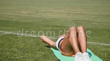 健身妇女在体育场做仰卧起坐锻炼。 运动女孩在户外腹部运动一名年轻成人