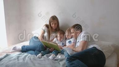 一家人的<strong>爸爸妈妈</strong>和两个双胞胎兄弟躺在床上看书。 家庭阅读时间。