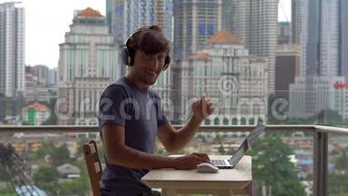年轻的自由职业者在阳台上的笔记本电脑上工作，背景是一个充满摩天大楼的市中心。 自由职业者