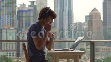 年轻的自由职业者在阳台上的笔记本电脑上工作，背景是一个充满摩天大楼的市中心。 自由职业者