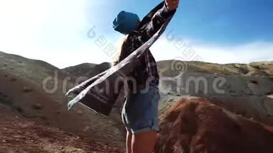 穿着花纹外套的年轻女游客站在红山的边缘，张开双臂作为翅膀。 她想