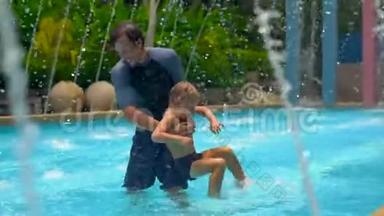一位年轻的父亲和他的儿子在喷泉间的一个热带水池里玩得很开心