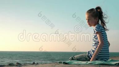 美丽的金发小女孩穿着条纹T恤，坐在海滩上，刮风的一天，科普空间概念，健康。