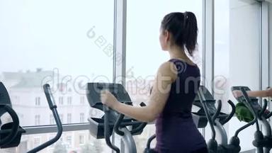 运动女孩在有大窗户的健身房运动模拟器上训练腿部肌肉