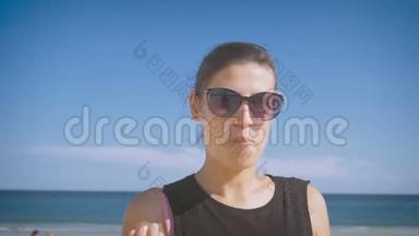 戴着太阳镜的女孩在海边吃葡萄，笑着竖起大拇指