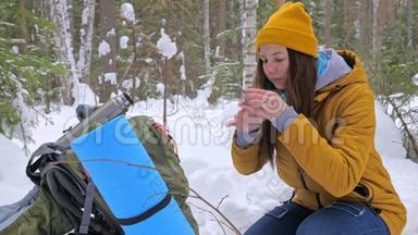 女孩游客在冬天白雪覆盖的森林里喝着热水瓶里的茶。