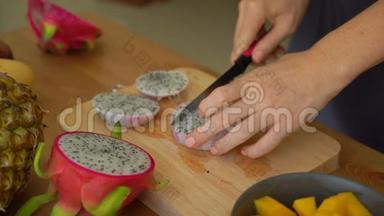慢镜头：一位年轻女子将火龙果切成方块，许多热带水果摆在桌上