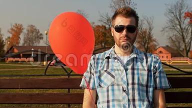 一个满脸胡须的人手里拿着一个红色<strong>气球坐</strong>在长凳上