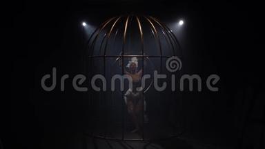 体操运动员在一个金笼里的箍上旋转。 黑烟背景。 慢动作