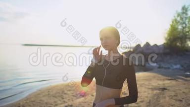 带着智能手表在海上慢跑的年轻女人。 年轻的运动女孩在日落时在海滩上使用智能手表。 太阳透镜耀斑