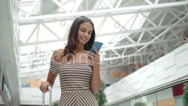 快乐的年轻女人在购物中心使用智能手机。 机场候机楼内有智能手机的女商务自由职业者