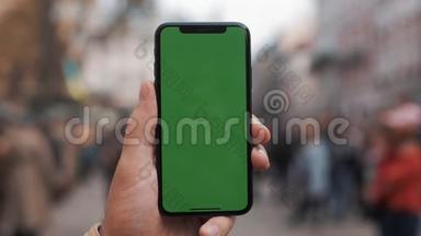 一名男子手持一部移动电话的特写镜头，街道上有一个垂直的绿色<strong>屏</strong>幕。<strong>大屏</strong>幕。军事