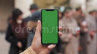 一名男子手持一部移动电话的特写镜头，街道上有一个垂直的绿色屏幕。大屏幕。军事